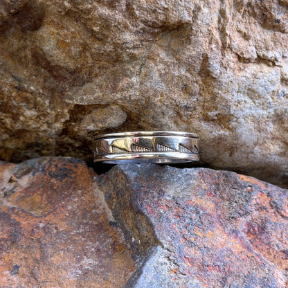 A silver band ring with a geometric chevron pattern sits nestled between textured orange and brown rocks.