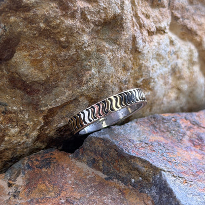 A silver ring with a wavy pattern resting on stacked natural rocks.