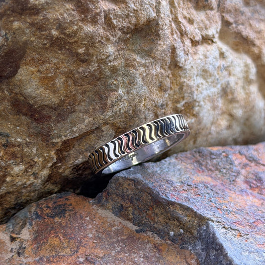 A silver ring with a wavy pattern resting on stacked natural rocks.