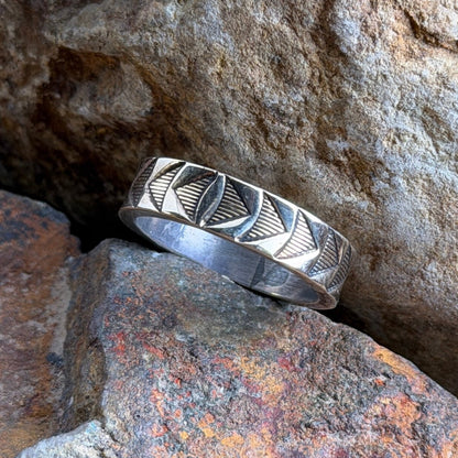 A silver geometric band ring resting on textured orange and gray rocks.