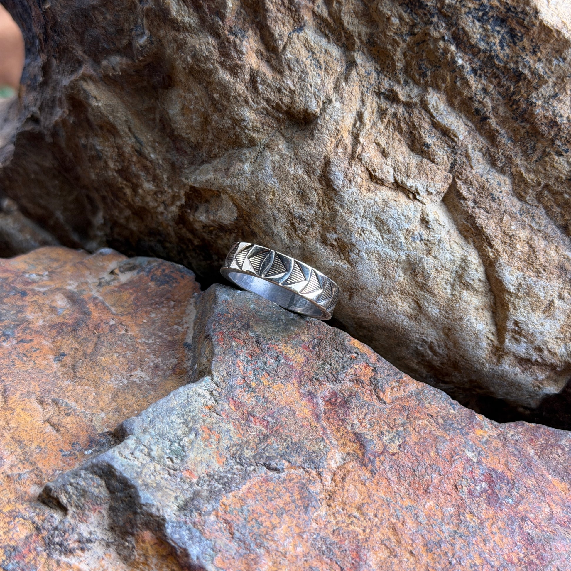 A 14k and sterling silver geometric band ring, resting on a textured orange-brown rock against a larger brown rock background.