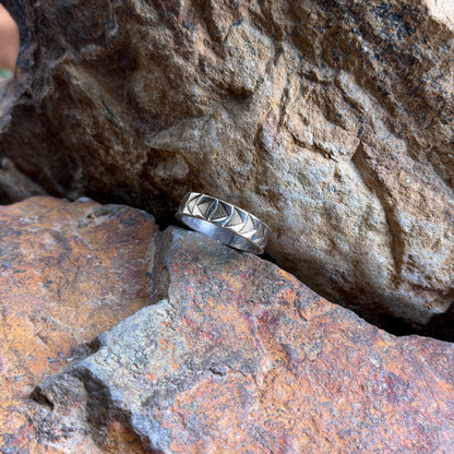 A 14k and sterling silver geometric band ring, resting on a textured orange-brown rock against a larger brown rock background.
