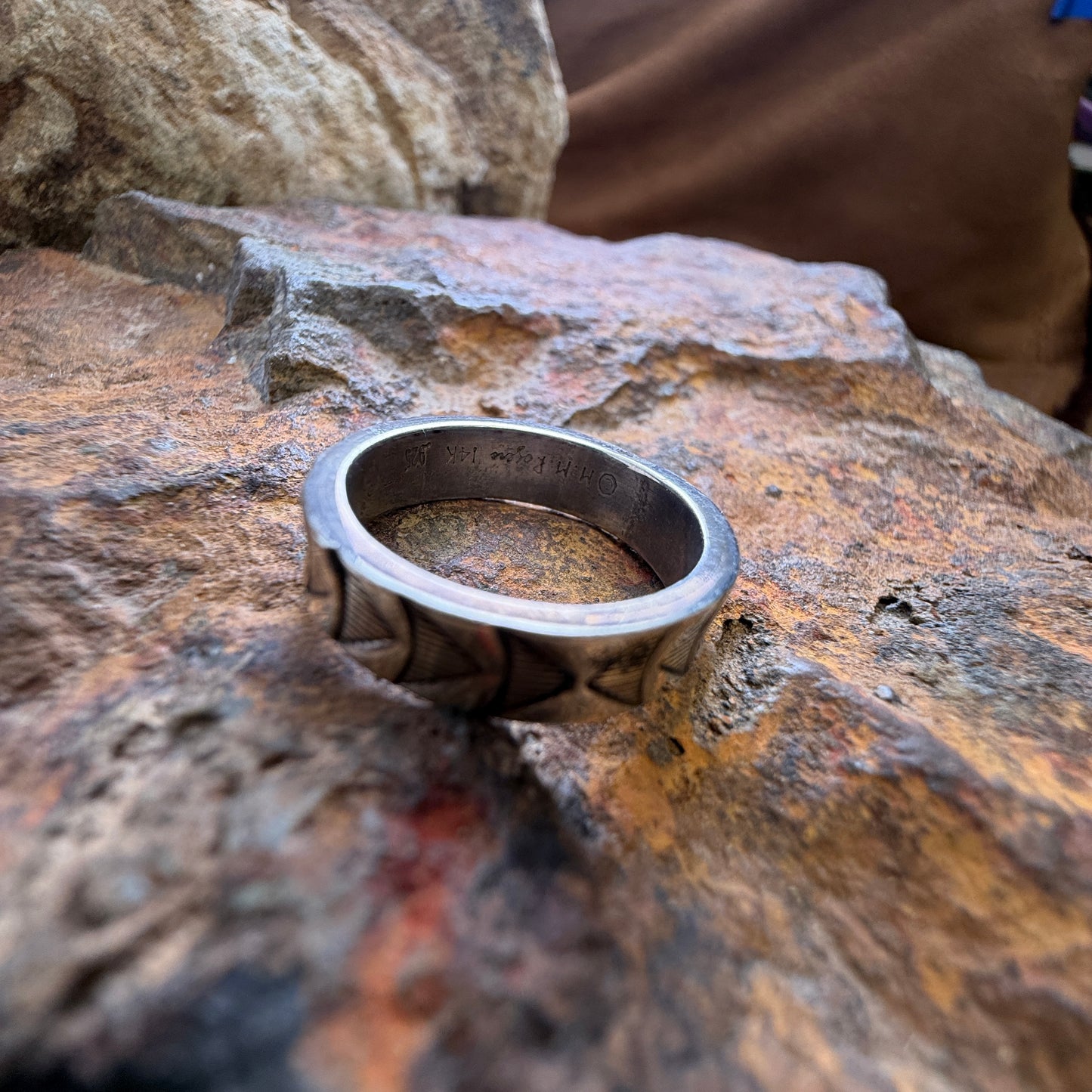 Inside hallmark MM Rodgers - 14k and sterling silver geometric band ring, resting on a textured orange-brown rock against a larger brown rock background.
