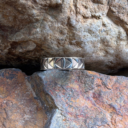 A 14k and sterling silver geometric band ring, resting on a textured orange-brown rock against a larger brown rock background.