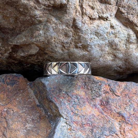 A 14k and sterling silver geometric band ring, resting on a textured orange-brown rock against a larger brown rock background.