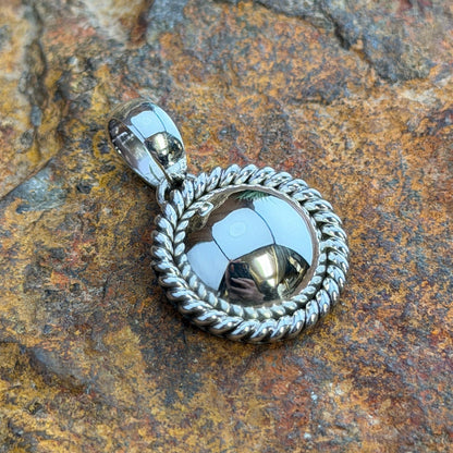  A pendant with a looped bail. A polished sterling silver dome is framed by a hand-twisted rope border