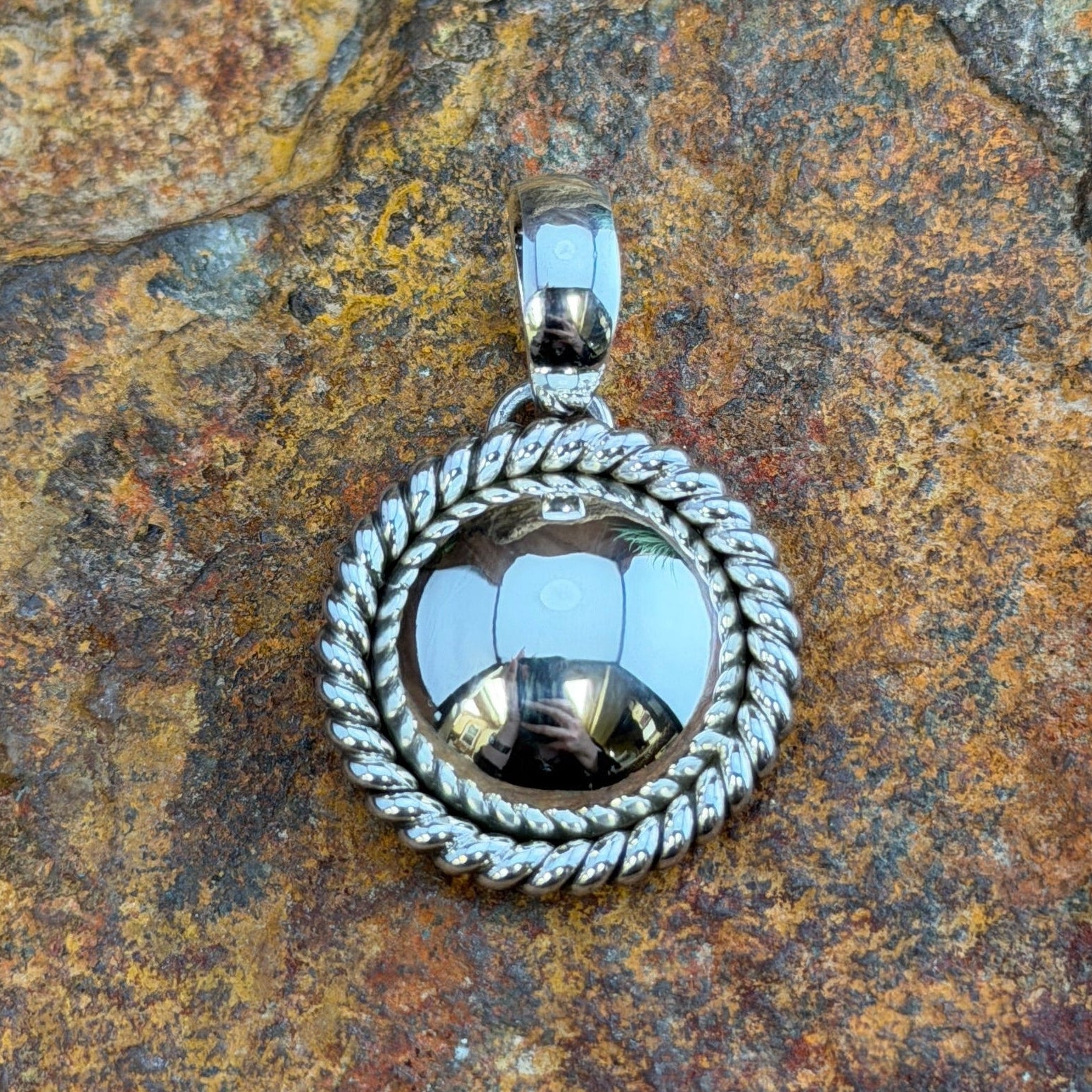  A pendant with a looped bail. A polished sterling silver dome is framed by a hand-twisted rope border