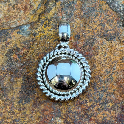  A pendant with a looped bail. A polished sterling silver dome is framed by a hand-twisted rope border