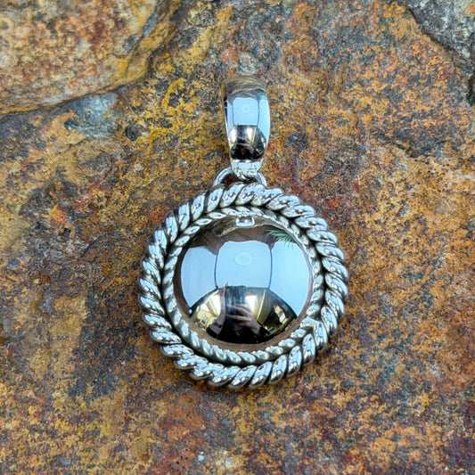  A pendant with a looped bail. A polished sterling silver dome is framed by a hand-twisted rope border
