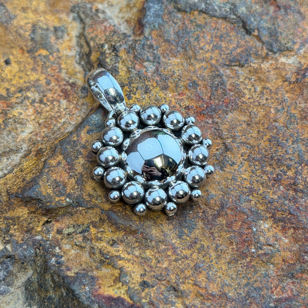 A polished domed sterling silver Pendant, its center is completely encircled by two concentric rows of bold and luminous all-silver pendant handcrafted by Navajo artist Artie Yellowhorse, showcasing her signature Million Drop technique. and-soldered graduated sterling silver shot beads, radiating outward in a striking sunburst halo.