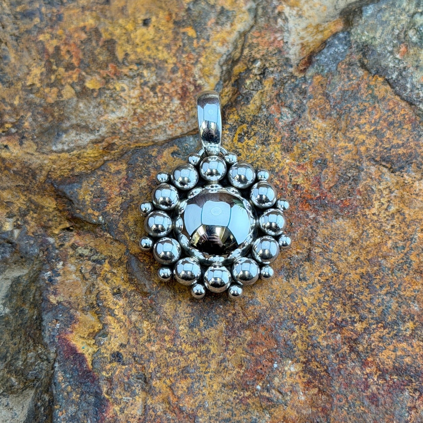A polished domed sterling silver Pendant, its center is completely encircled by two concentric rows of bold and luminous all-silver pendant handcrafted by Navajo artist Artie Yellowhorse, showcasing her signature Million Drop technique. and-soldered graduated sterling silver shot beads, radiating outward in a striking sunburst halo.
