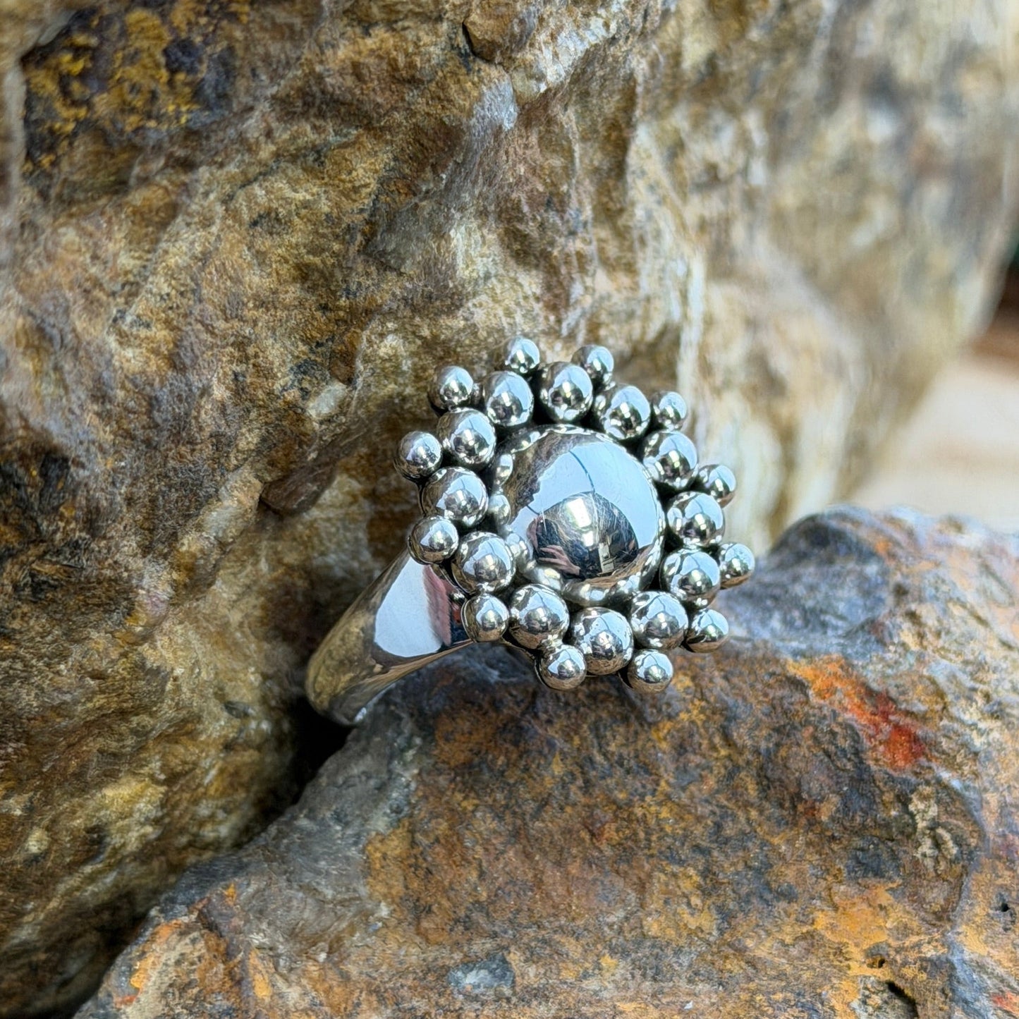 A polished sterling silver dome rises from the center, encircled by two concentric rings of hand-soldered silver shot beads radiating outward in a sunburst pattern.