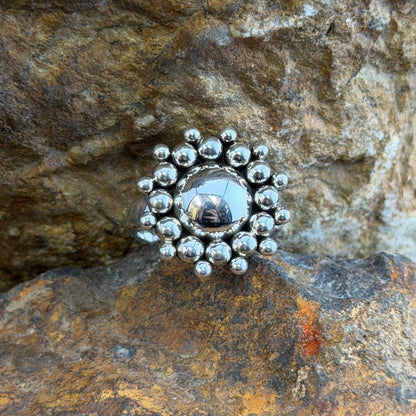  A polished sterling silver dome rises from the center, encircled by two concentric rings of hand-soldered silver shot beads that radiate outward in a sunburst pattern. 