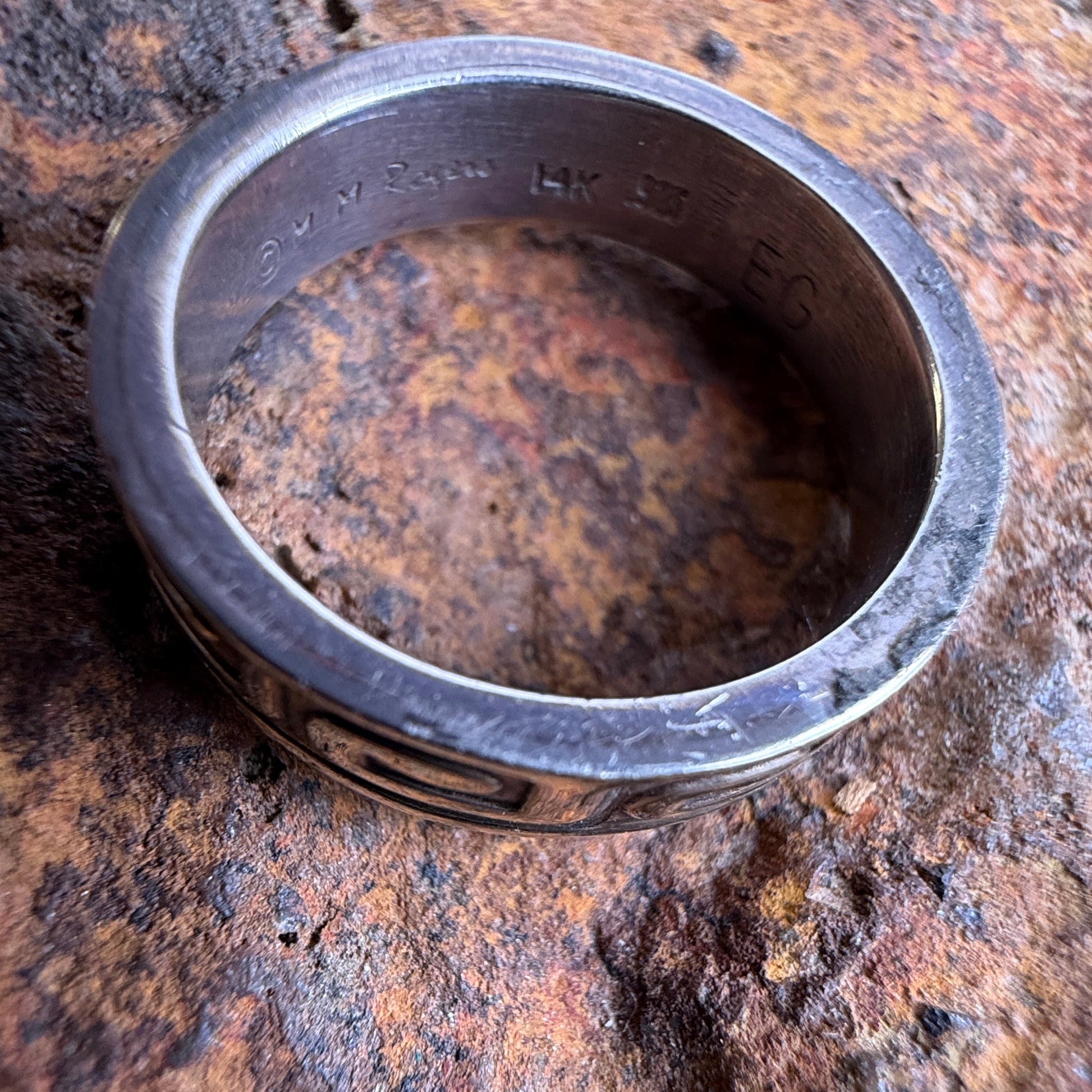 A sterling silver band ring with engraved lettering, resting on a textured, rocky brown surface.