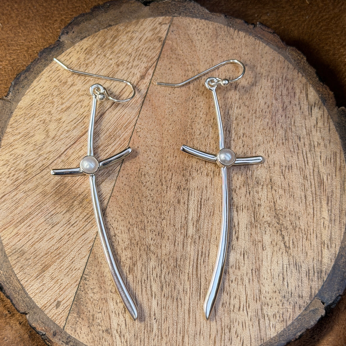 silver cross earrings with small pearl in center displayed on wood