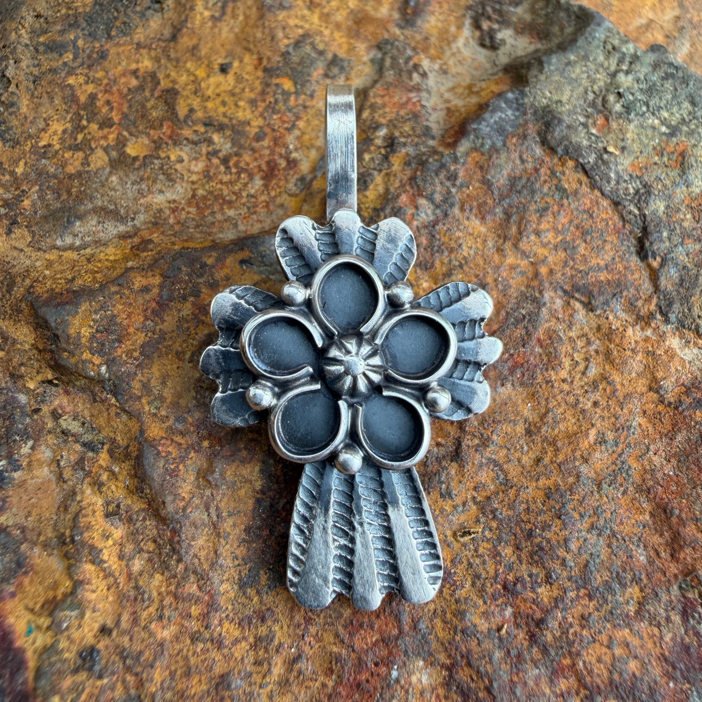 Silver floral cross pendant on a textured stone background
