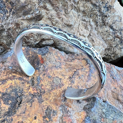 Silver bracelet with intricate designs on a rocky surface