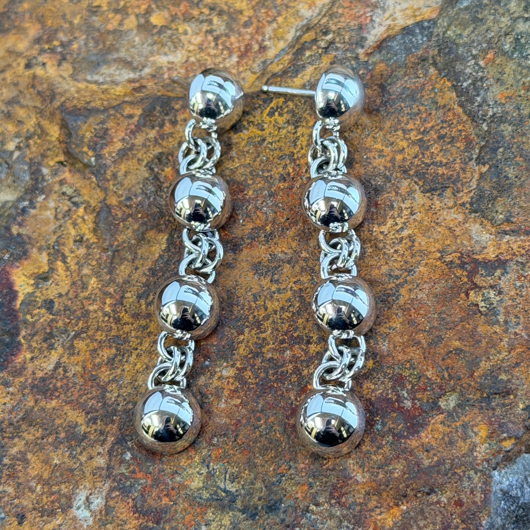 Sterling Silver Sphere and Byzantine Chain Dangle Earrings by Artie Yellowhorse - flat lay on rock showing four graduated spheres linked by Byzantine chain on ball posts