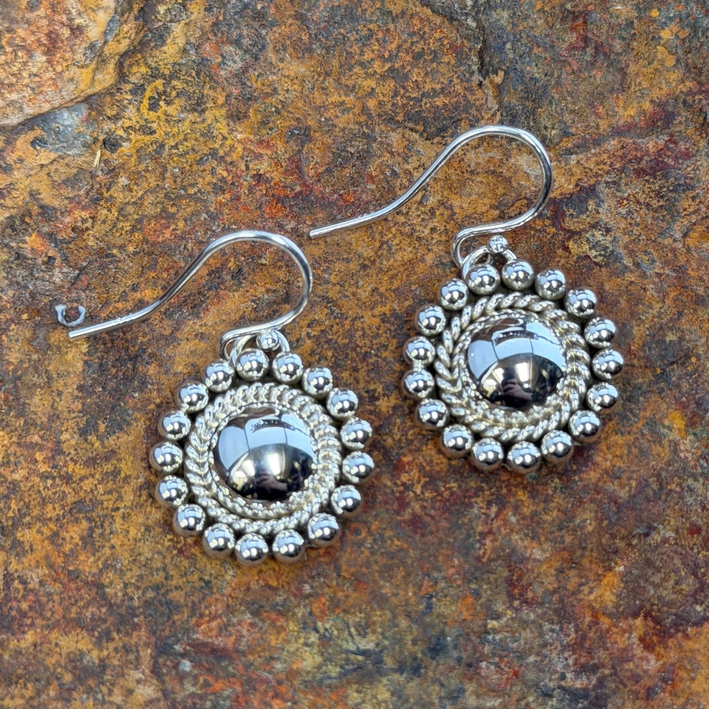 Sterling Silver Dome Rope and Sphere Dangle Earrings by Artie Yellowhorse - flat lay on rock showing domed center with twisted rope border and hand-applied sphere outer edge