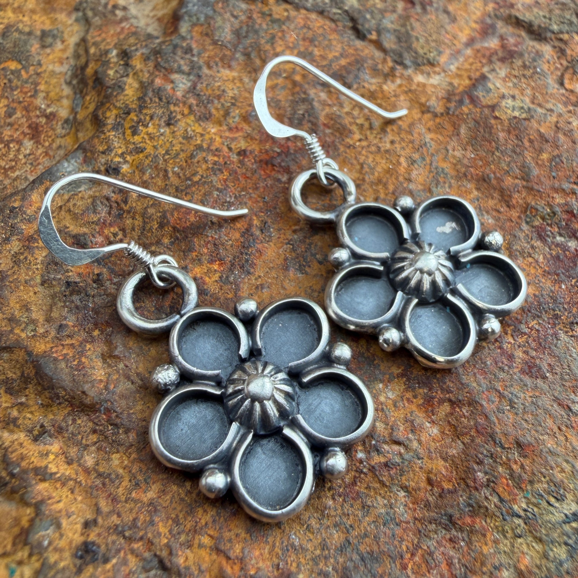Silver floral earrings on a textured stone surface