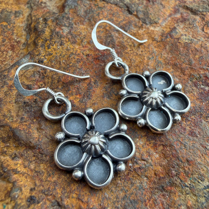 Silver floral earrings on a textured stone surface