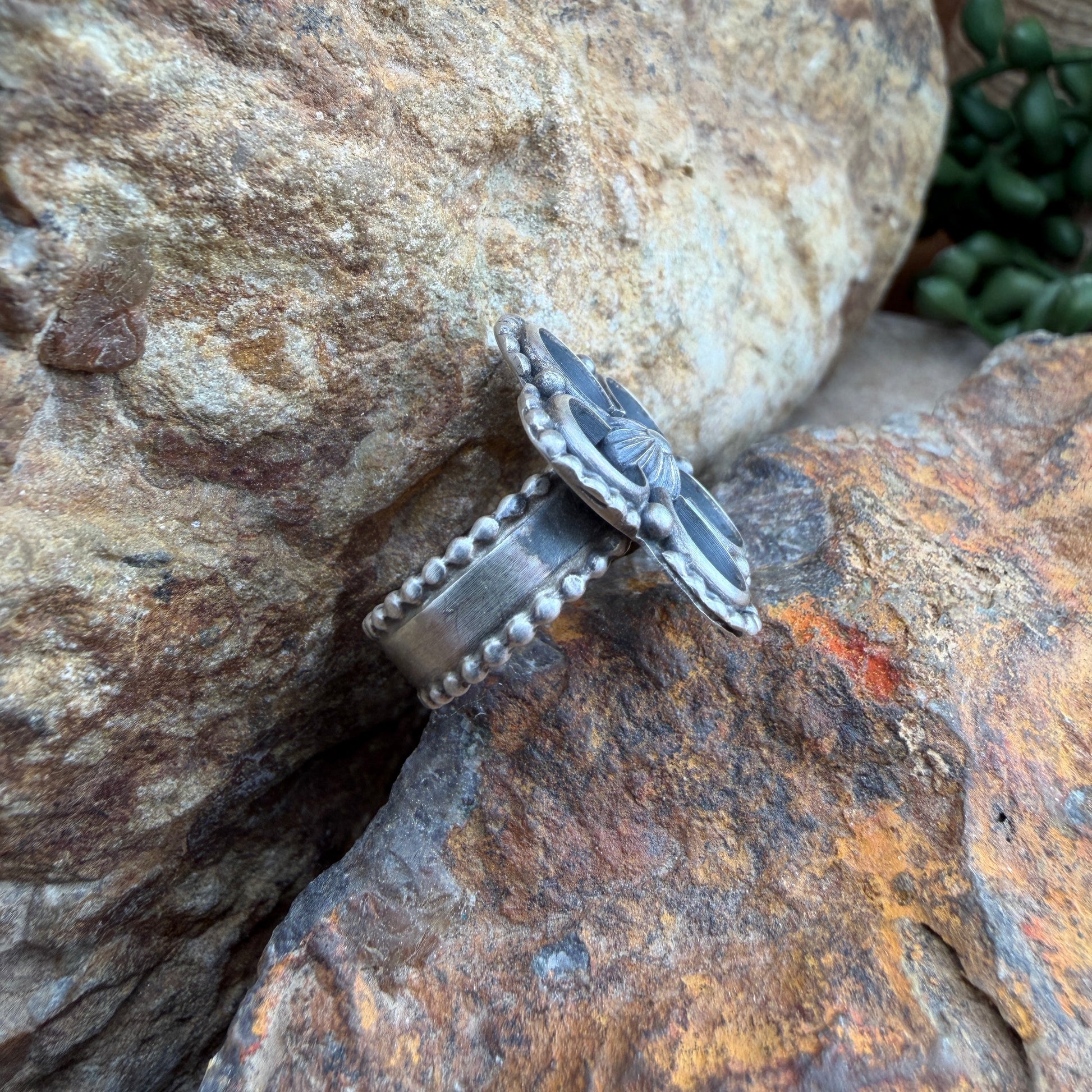 Silver ring with intricate design on a textured stone surface