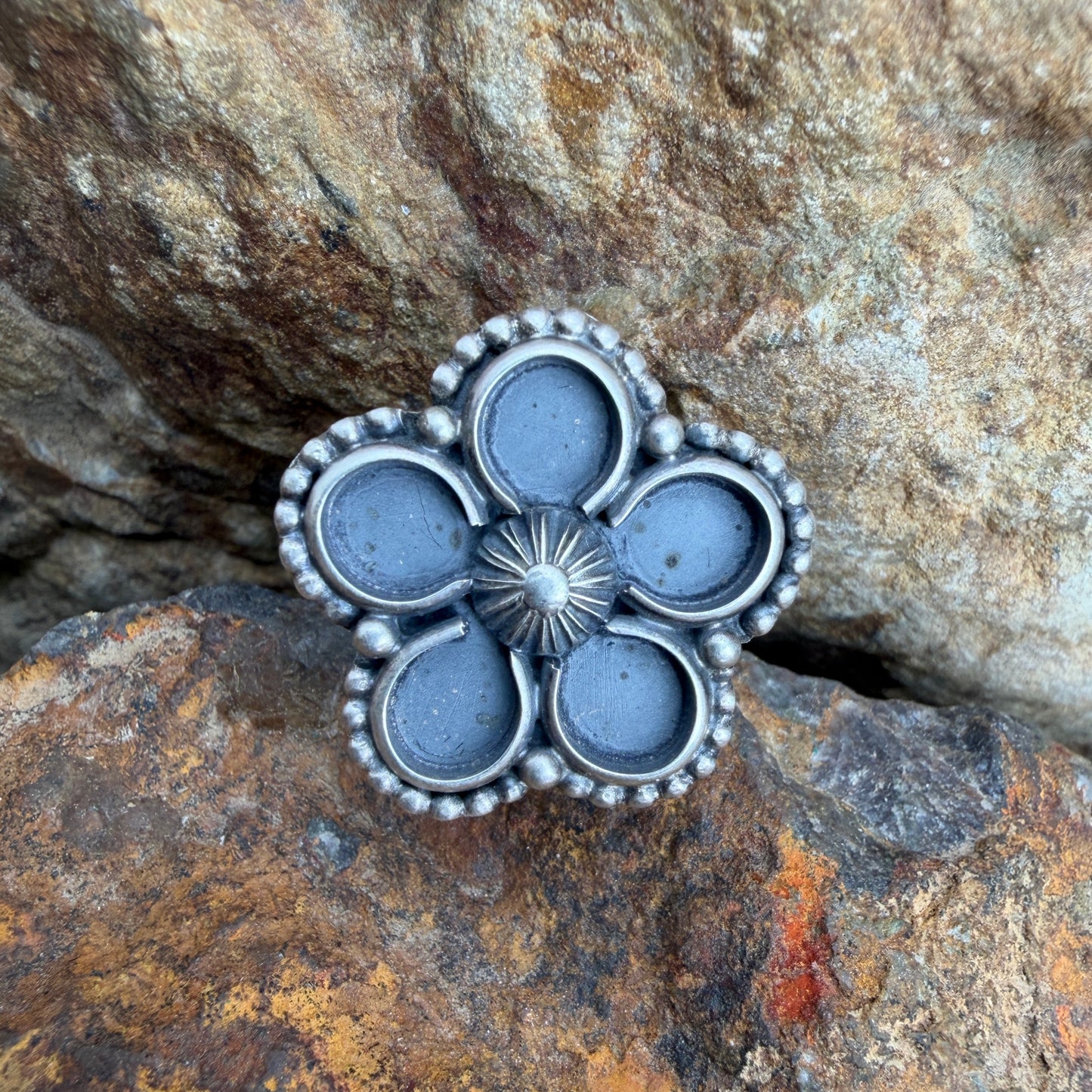 Silver flower-shaped ring on a rocky surface