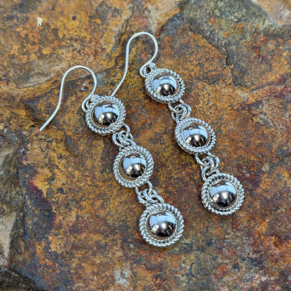 Sterling Silver Triple Drop Dangle Earrings by Artie Yellowhorse - flat lay on rock showing three graduated dome elements with twisted rope frames
