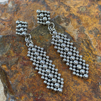 Sterling Silver Million Drop Post and Dangle Earrings by Artie Yellowhorse - flat lay on rock showing diamond post top and elongated oval drop covered in hand-soldered silver spheres