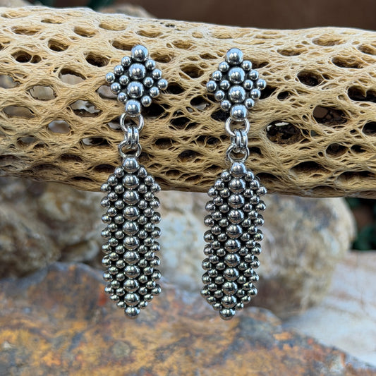 Post Drop earrings with a diamond shaped post embellished with Silver drops, an elongated diamond hangs from the posts. By artie yellowhorse. they hang from driftwood