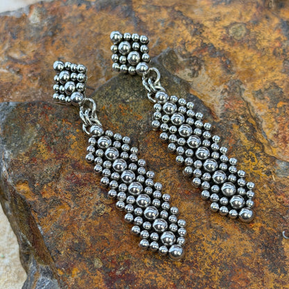 Post Drop earrings with a diamond shaped post embellished with Silver drops, an elongated diamond hangs from the posts. they rest on a rocky surface
