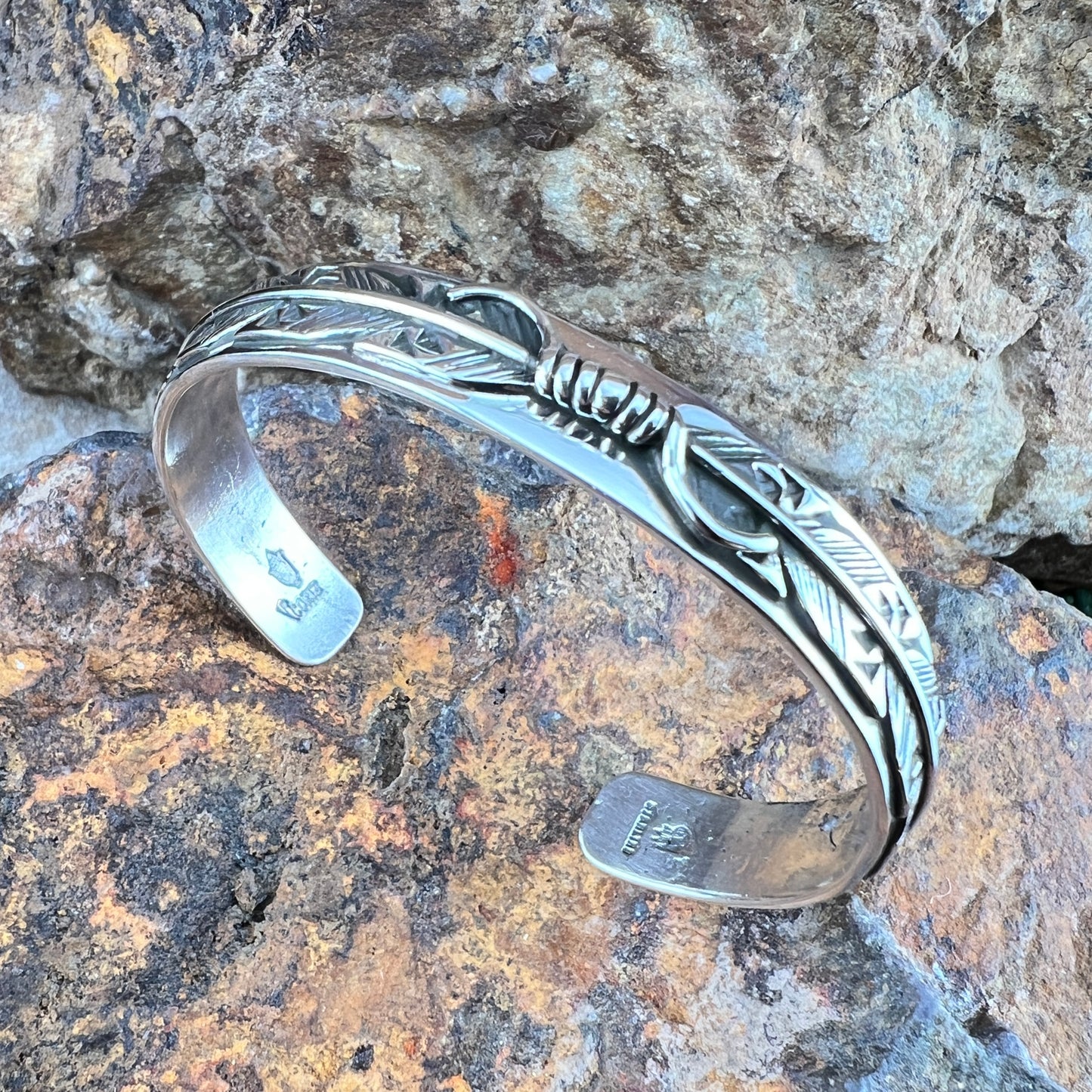 Silver bracelet with feather design on a textured stone surface