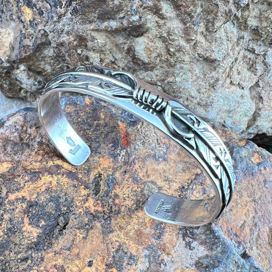 Silver bracelet with feather design on a textured stone surface