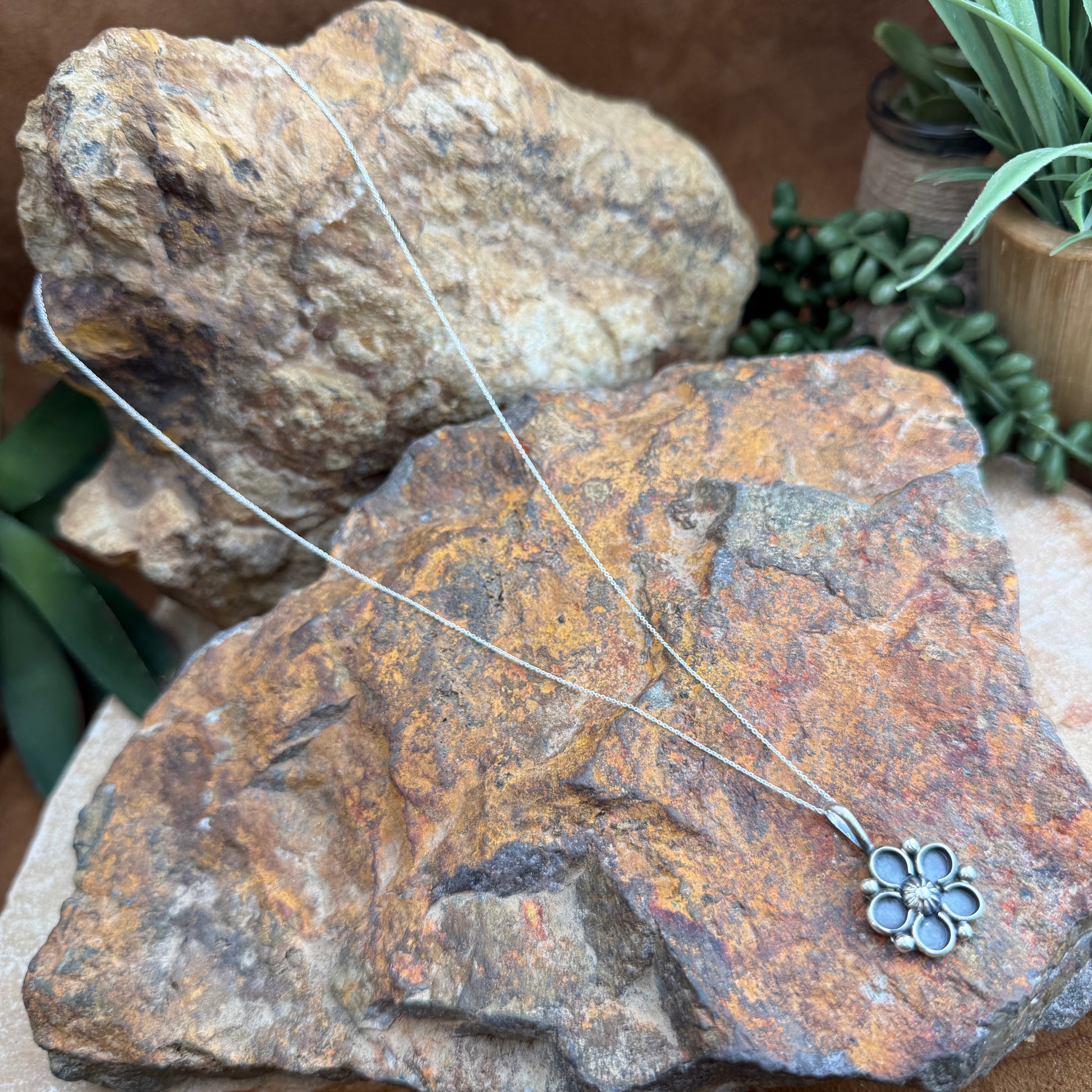 Silver necklace with a floral pendant on a textured stone surface