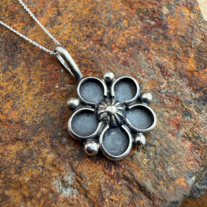 Silver floral pendant on a chain against a textured stone background