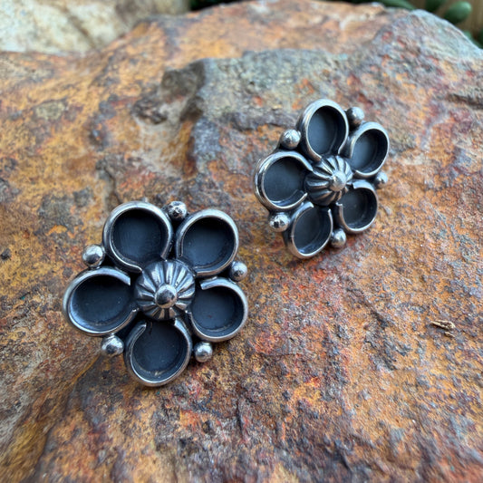 Pair of silver floral earrings on a textured stone surface