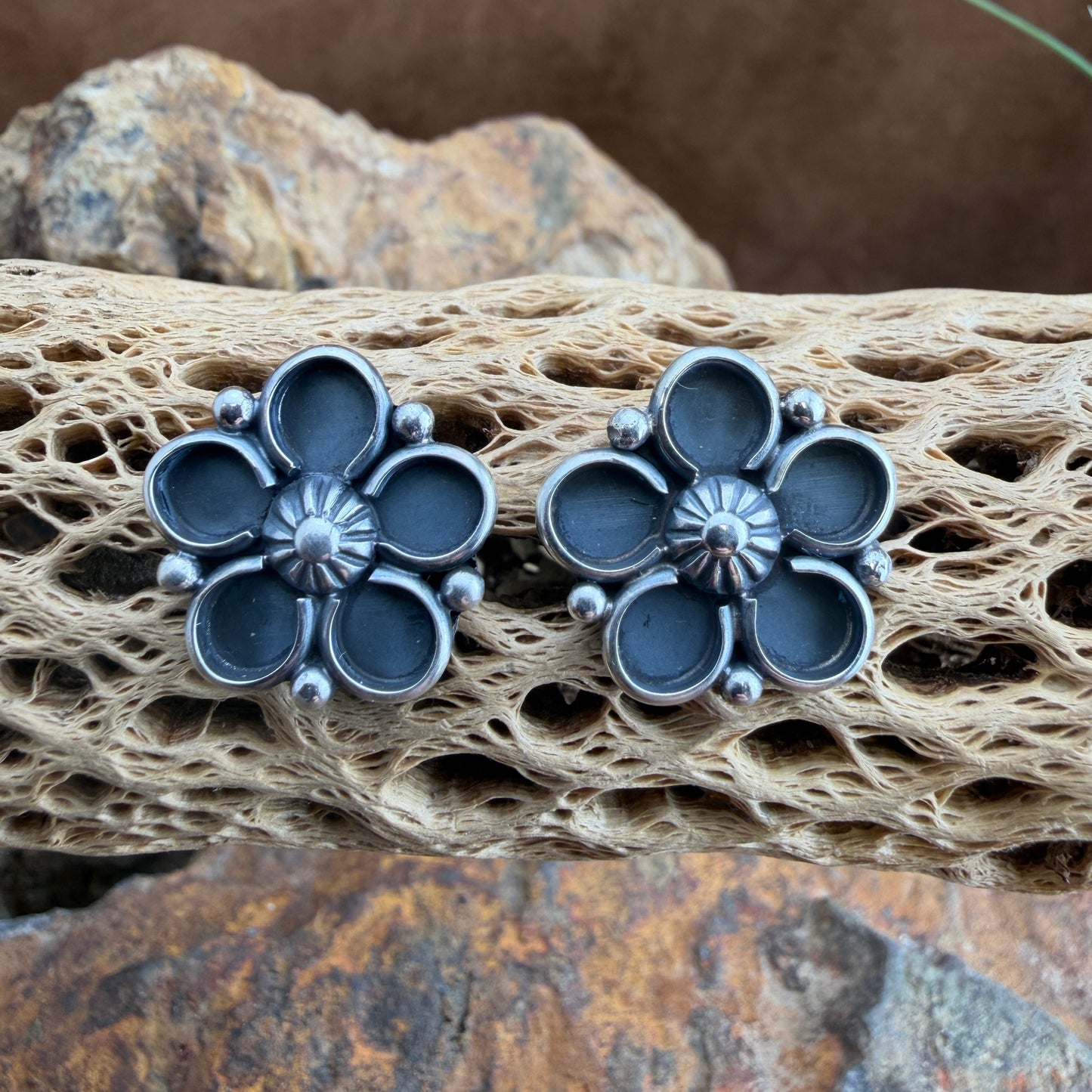 Pair of silver flower-shaped earrings on a textured stone surface
