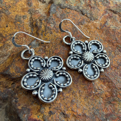 Silver floral earrings on a stone background