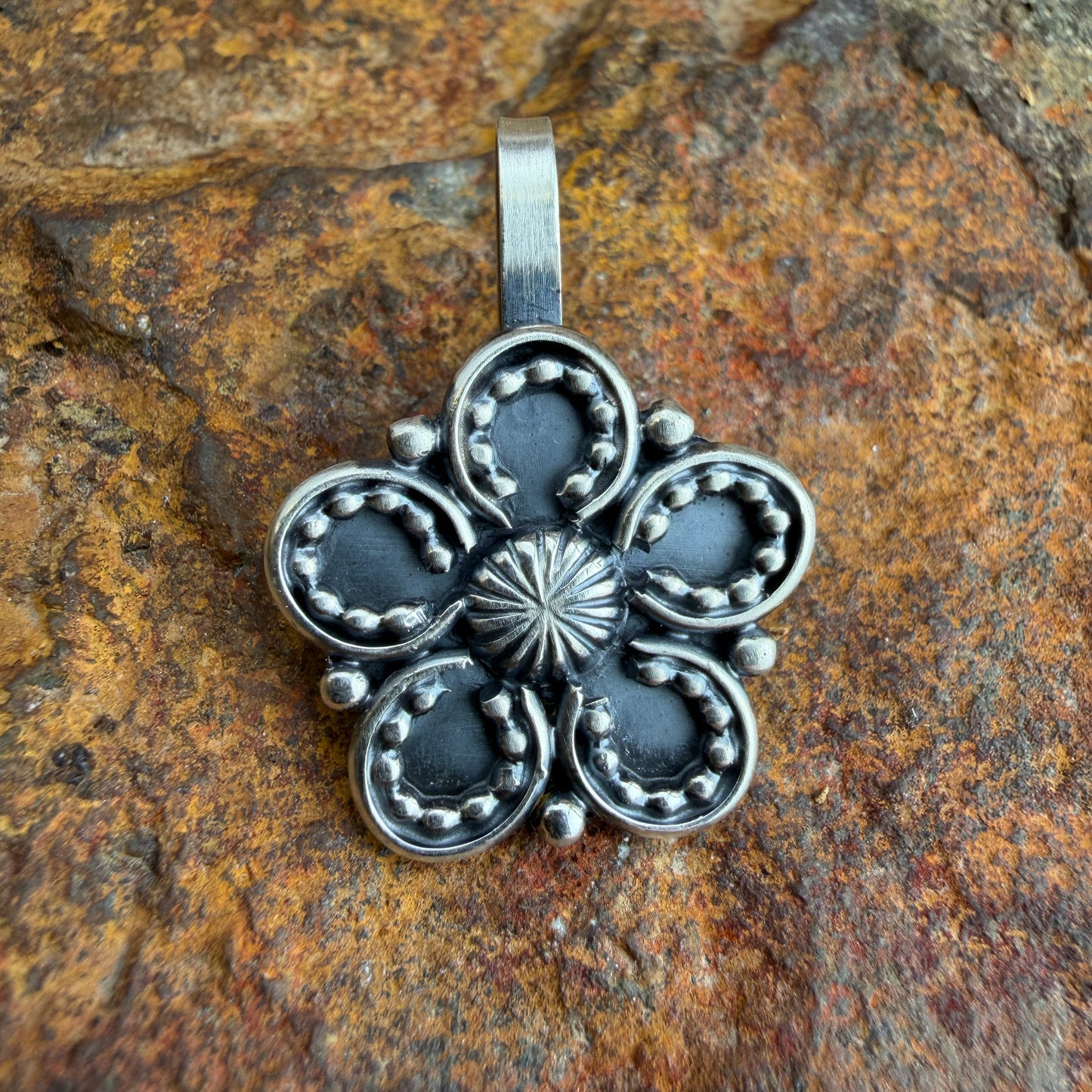 Silver floral pendant on a textured stone background
