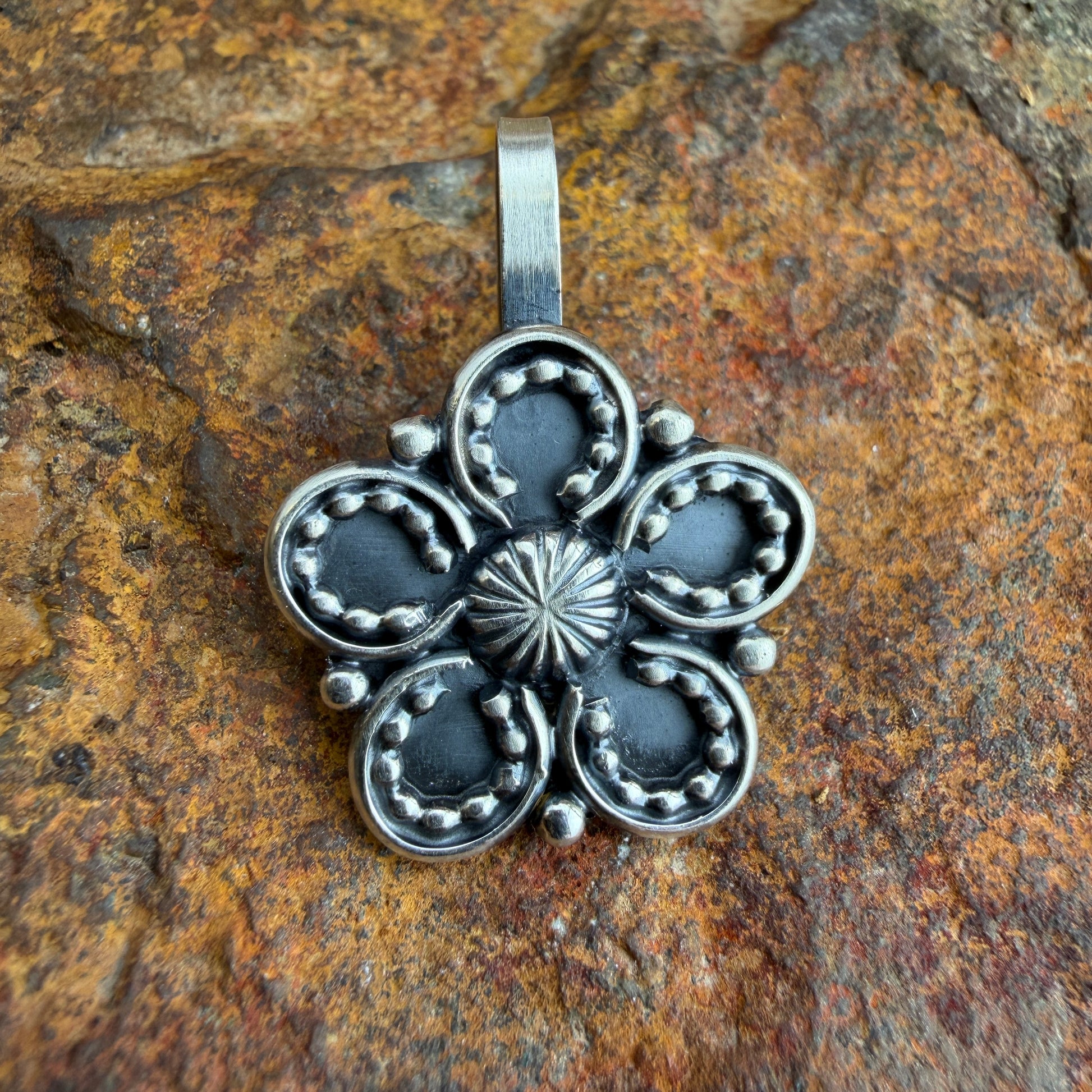 Silver floral pendant on a textured stone background