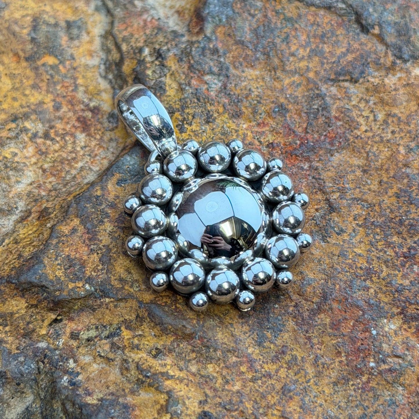 Sterling Silver Hematite Million Drop Pendant by Artie Yellowhorse - front view on rock showing faceted hematite center with double row silver sphere halo