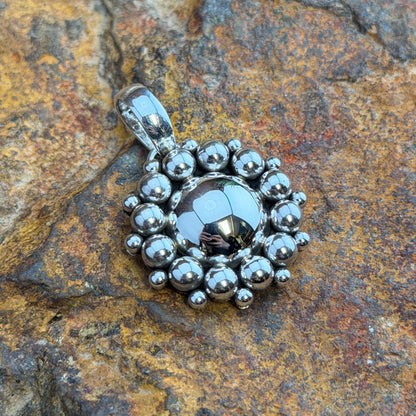 Sterling Silver Hematite Million Drop Pendant by Artie Yellowhorse - front view on rock showing faceted hematite center with double row silver sphere halo