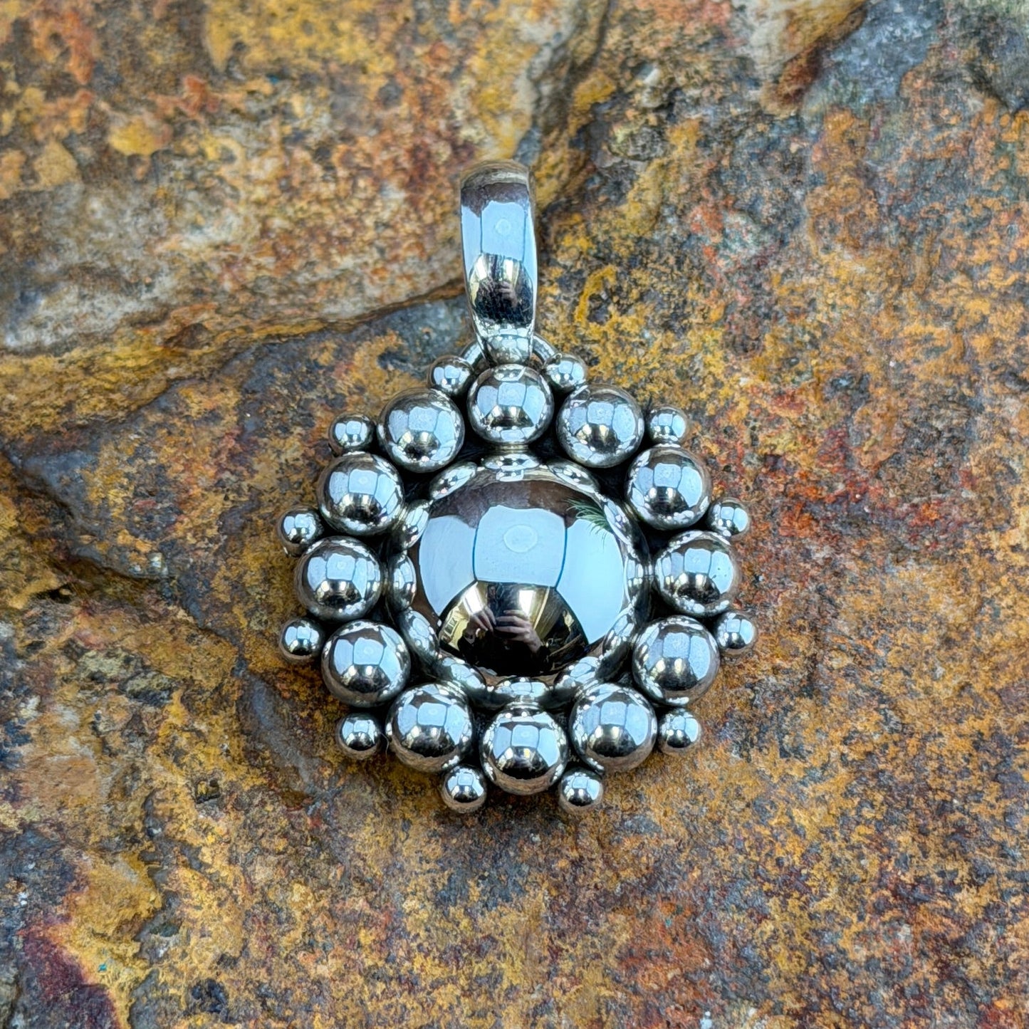 Sterling Silver Million Drop Pendant by Artie Yellowhorse - angled front view on rock showing scalloped outer edge and polished bail