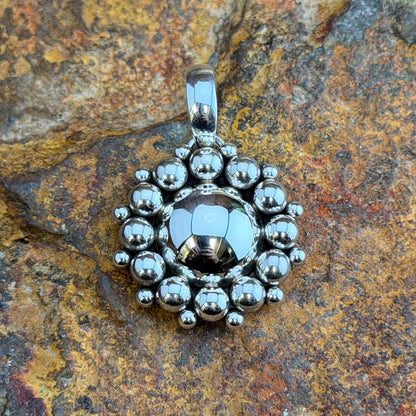 Sterling Silver Million Drop Pendant by Artie Yellowhorse - angled front view on rock showing scalloped outer edge and polished bail