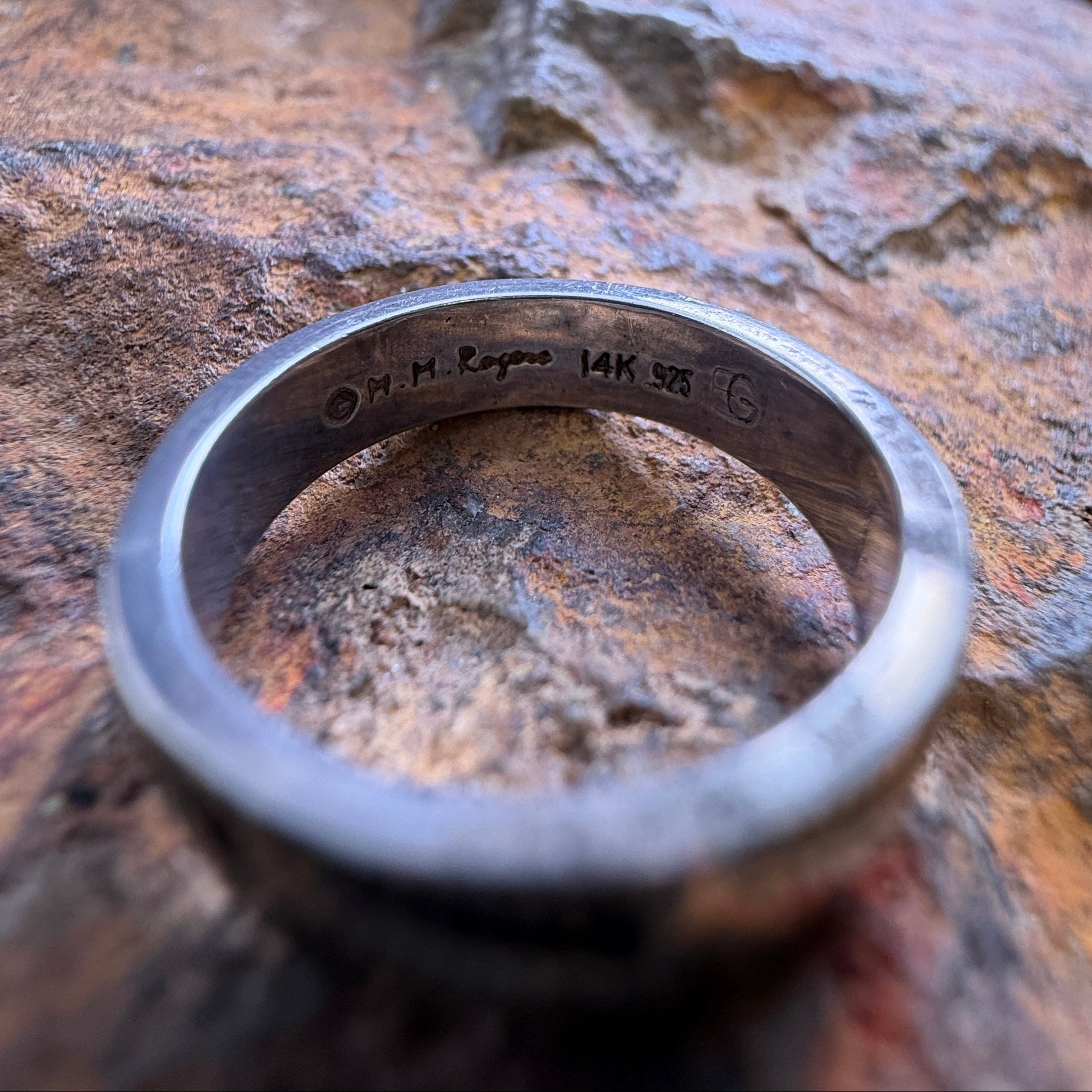 A silver ring with engraved markings inside, resting on a textured brown rock surface.