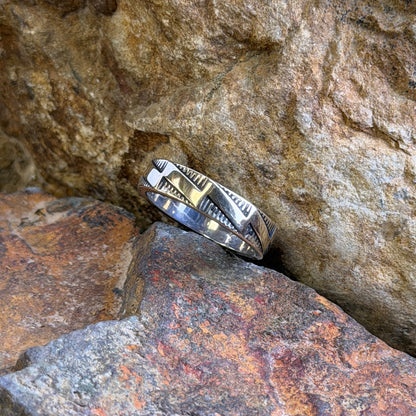 a silver and gold  band with hatched markings and stepped accents sitting in-between two rocks