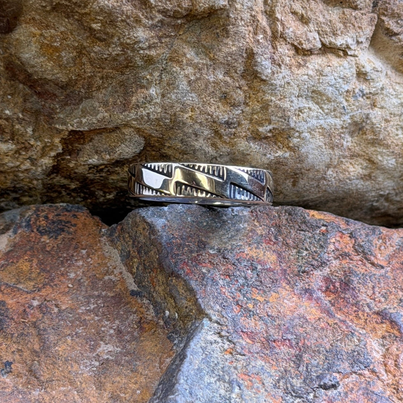 A silver and gold ring with stepped accents against a hatched background