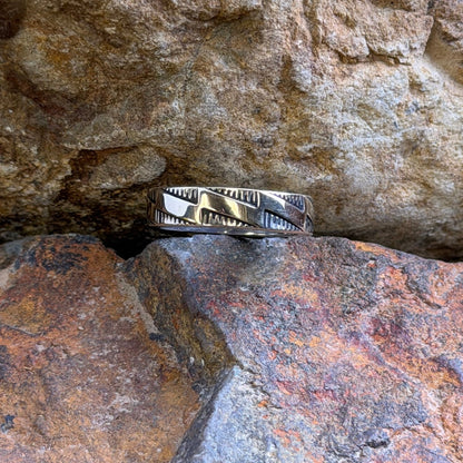 A silver and gold ring with stepped accents against a hatched background