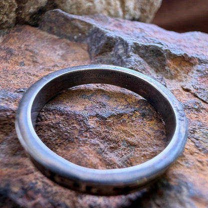 A polished silver and gold band sitting on a rock. it features stamping on the inside. 
