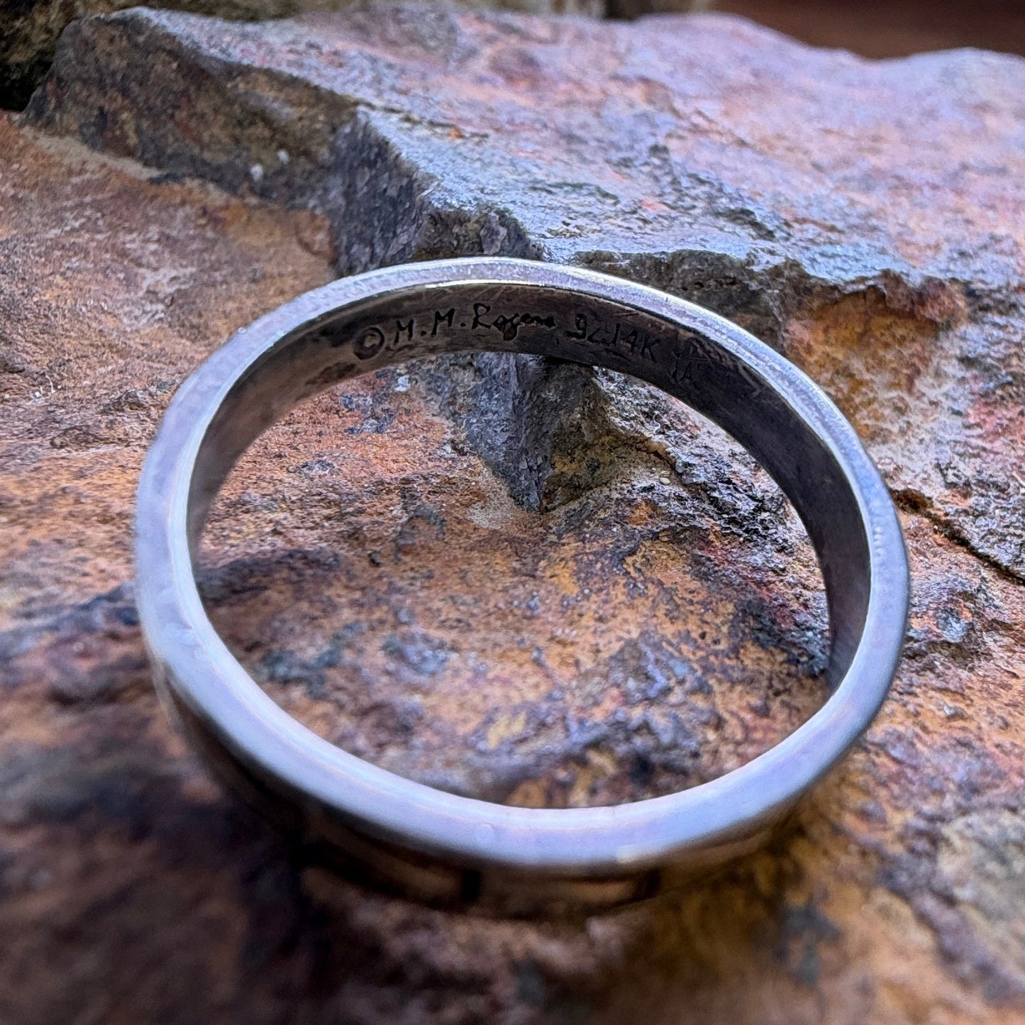 A sterling silver and 14k gold ring sitting on a rocky surface showcasing the stamping on the inside